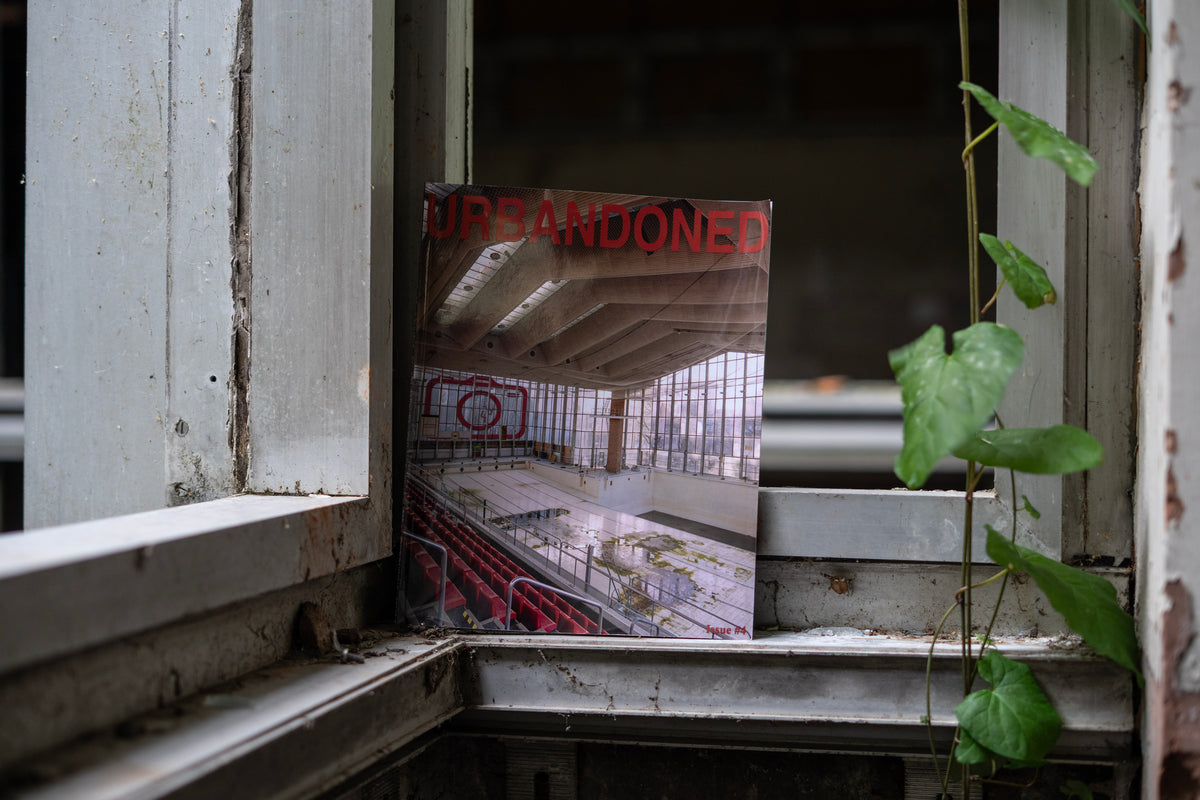Urbandoned Issue 4 standing on a peeling window ledge beside trailing ivy
